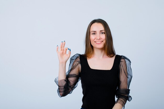 Smiling young girl is showing okay gesture on white background