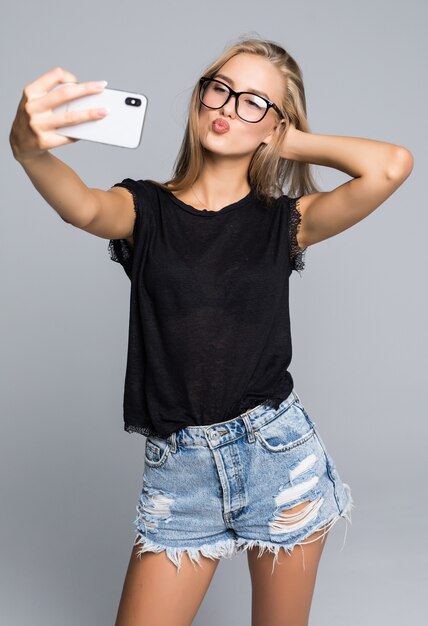 Smiling young girl making selfie photo on smartphone over gray background