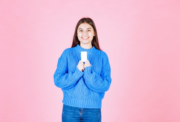 smiling young girl model holding a card on pink wall.