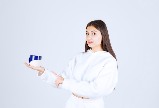 Sorridente ragazza che punta a una tazza su sfondo bianco-grigio.