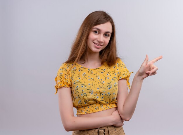 Smiling young girl pointing at right side on isolated white wall with copy space