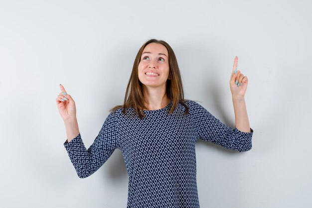 Smiling young girl points her fingers to the top on a white background