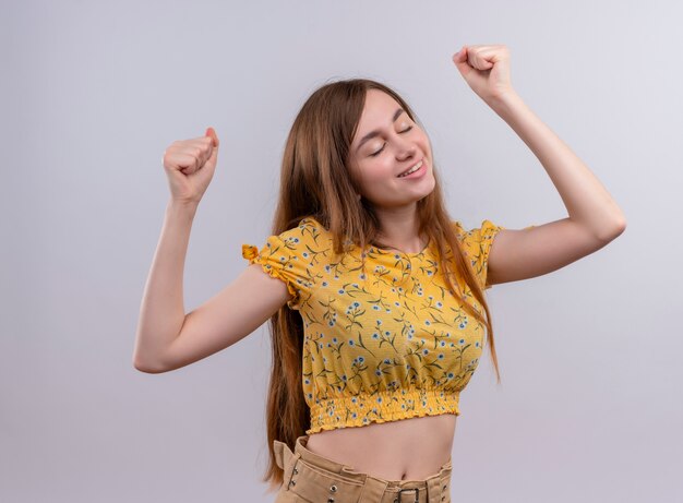 Smiling young girl raising fists with closed eyes on isolated white wall