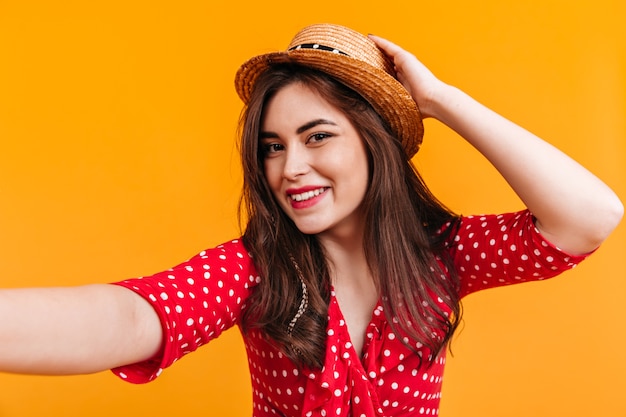 La ragazza sorridente in cima a pois rossi e alle imbarcazioni fa selfie sulla parete gialla.