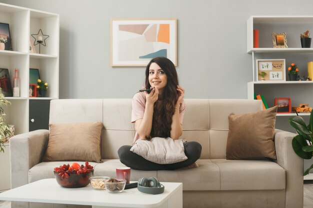 Smiling young girl speaks on phone sitting on sofa behind coffee table in living room