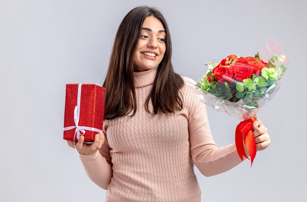 흰색 배경에 고립 된 그녀의 손에 꽃다발을보고 선물 상자를 들고 발렌타인 데이에 웃는 어린 소녀