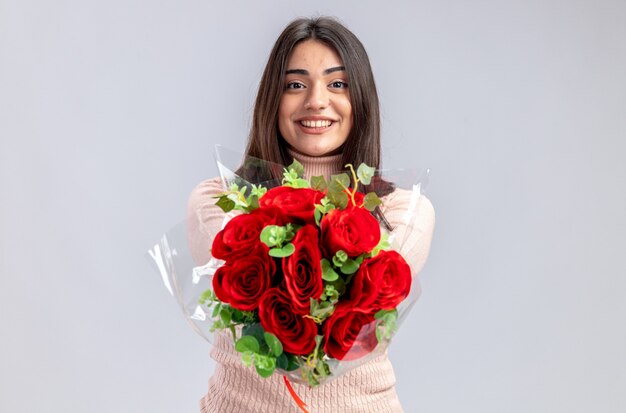 Smiling young girl on valentines day holding out bouquet at camera isolated on white background