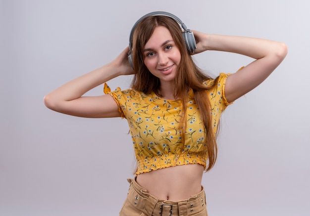 Smiling young girl wearing headphones and putting hands behind head on isolated white wall