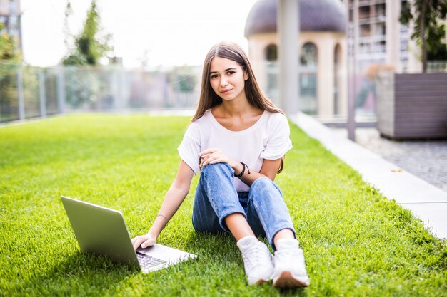 야외 잔디에 앉아 노트북과 웃는 어린 소녀