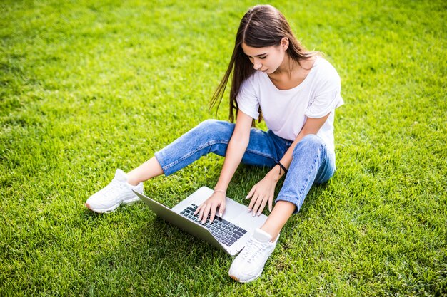 屋外の芝生の上に座っているラップトップを持つ笑顔の少女
