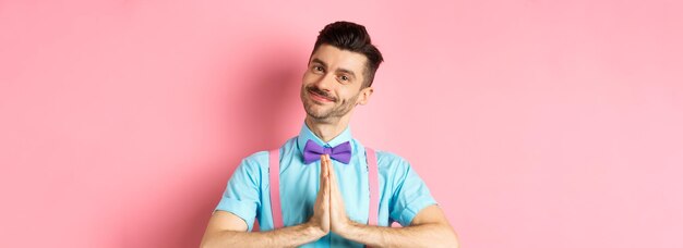 Free photo smiling young guy in bowtie say thank you looking with gratitude and holding hands in namaste gestur