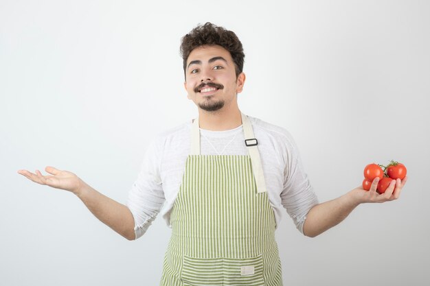 Smiling young guy holding fresh tomatoes and holding his arms up.