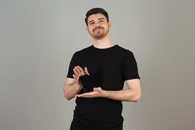 Smiling young guy holding phone with both hands and looking at camera.