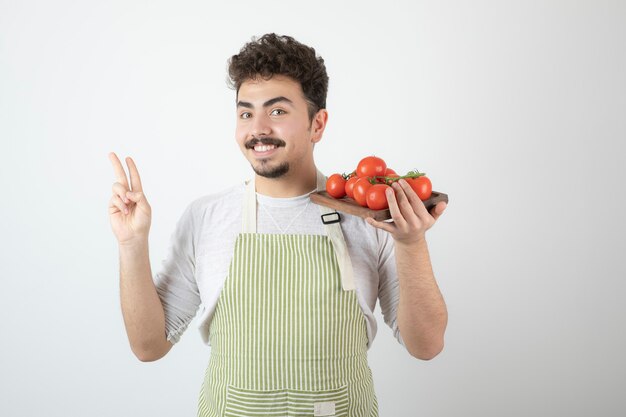 Smiling young guy holding pile of red tomatoes.