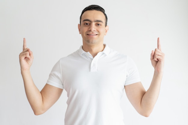 Smiling young guy pointing upwards and looking at camera