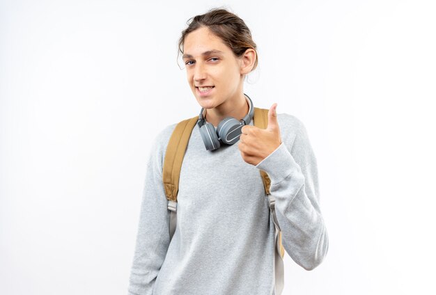 Улыбающийся молодой парень студент носить рюкзак с наушниками на шее, показывая большой палец вверх