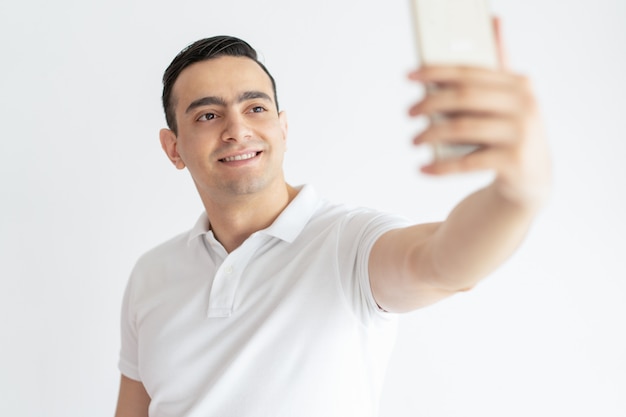 Smiling young guy taking selfie photo on smartphone