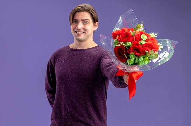 青い背景で隔離のカメラで花束を差し出してバレンタインデーに笑顔の若い男