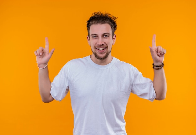 白いTシャツを着て笑顔の若い男は、孤立したオレンジ色の背景の上を指しています