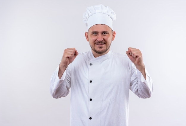 흰색 공간에 고립 된 떨리는 주먹으로 요리사 유니폼에 젊은 잘 생긴 요리사 미소