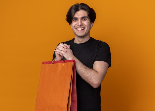 Free photo smiling young handsome guy wearing black t-shirt holding bag isolated on orange wall