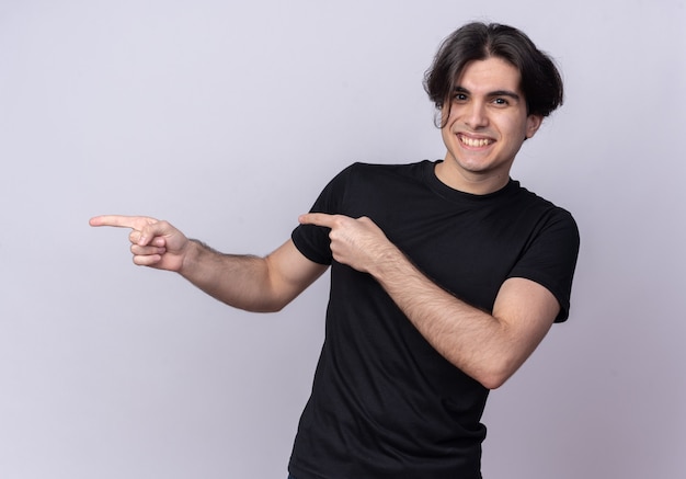 Smiling young handsome guy wearing black t-shirt points at side isolated on white wall with copy space