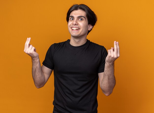Smiling young handsome guy wearing black t-shirt showing tip gesture isolated on orange wall