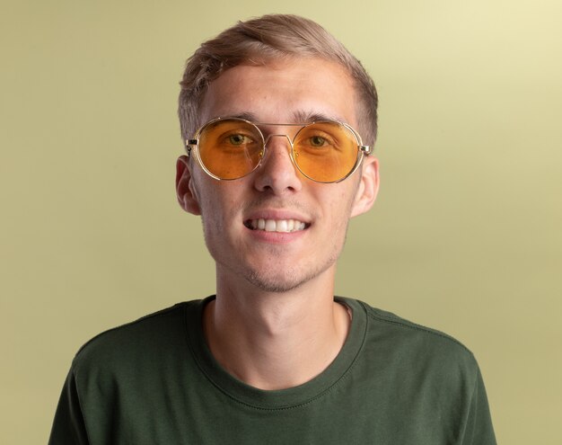 Smiling  young handsome guy wearing green shirt with glasses isolated on olive green wall