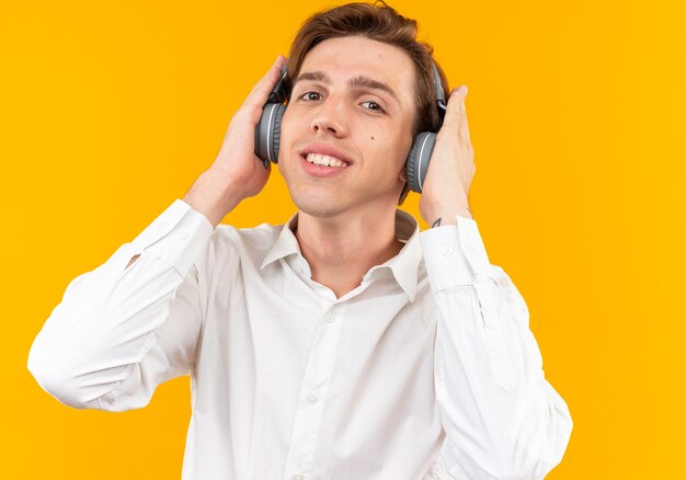 Smiling young handsome guy wearing white shirt with headphones isolated on orange wall