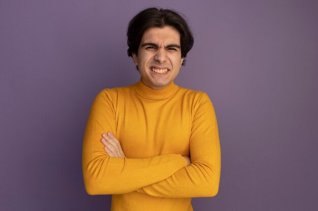 보라색 벽에 고립 된 손을 건너 노란색 터틀넥 스웨터를 입고 웃는 젊은 잘 생긴 남자
