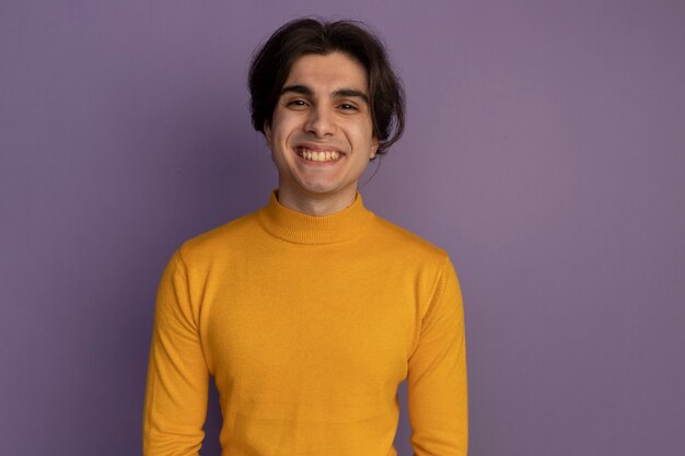 Smiling young handsome guy wearing yellow turtleneck sweater isolated on purple wall with copy space