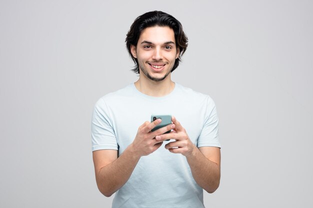 smiling young handsome man holding mobile phone with both hands looking at camera isolated on white background