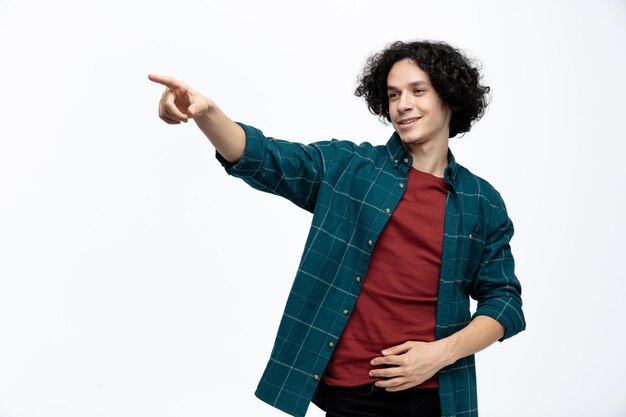 Smiling young handsome man keeping hand on belly looking and pointing at side isolated on white background