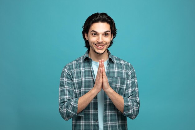 smiling young handsome man looking at camera showing namaste gesture isolated on blue background