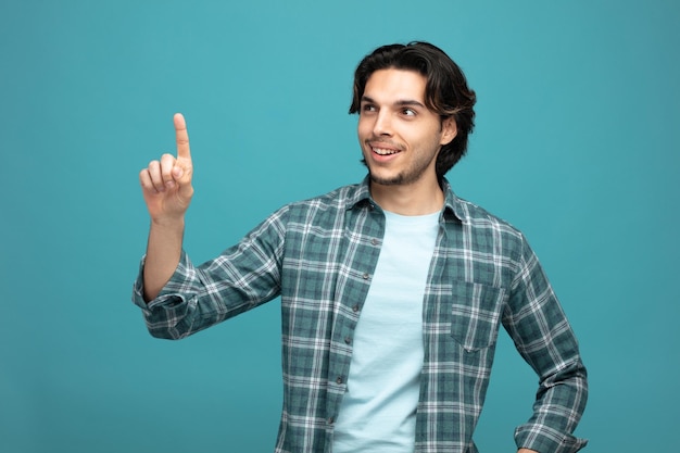 smiling young handsome man looking at side pointing up isolated on blue background