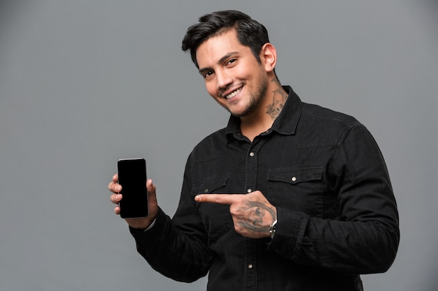 Smiling young handsome man pointing to display of mobile phone.