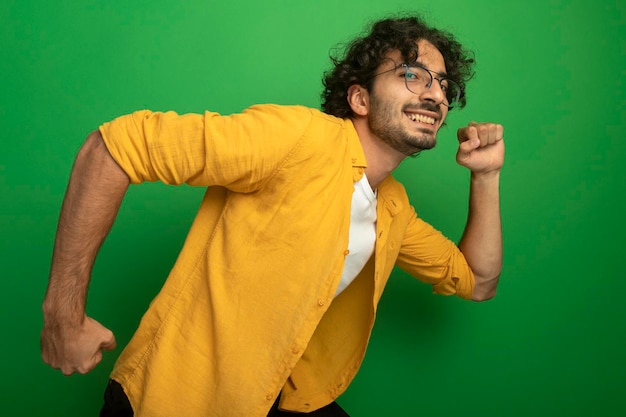 Free photo smiling young handsome man wearing glasses looking at front clenching fists running isolated on green wall