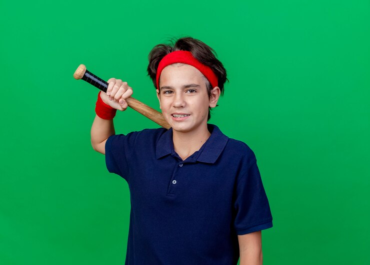 मुफ़्त फोटो smiling young handsome sporty boy wearing headband and wristbands with dental braces looking at camera holding baseball bat isolated on green background with copy space