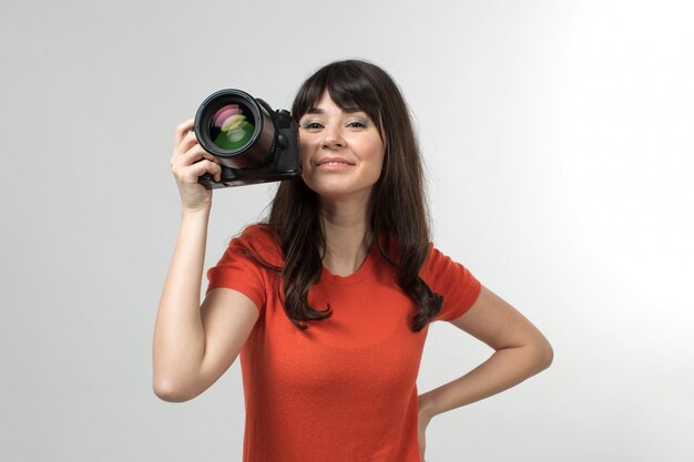 smiling young lady holding photocamera in designed t-shirt in good mood with long hair on white