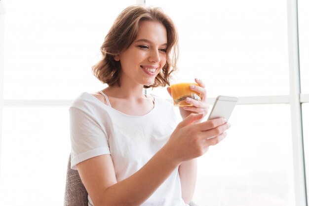 ジュースを飲むウィンドウのそばに座って笑顔の若い女性