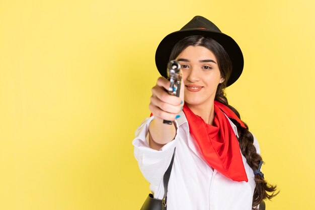 Улыбающаяся юная леди, стоящая на желтом фоне и направляющая пистолет в камеру Высококачественное фото