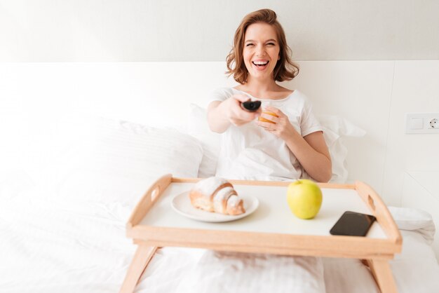 Smiling young lady watch tv holding remote control.