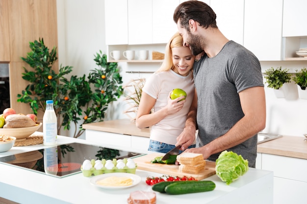 Smiling young loving couple standing at kitchen and cooking