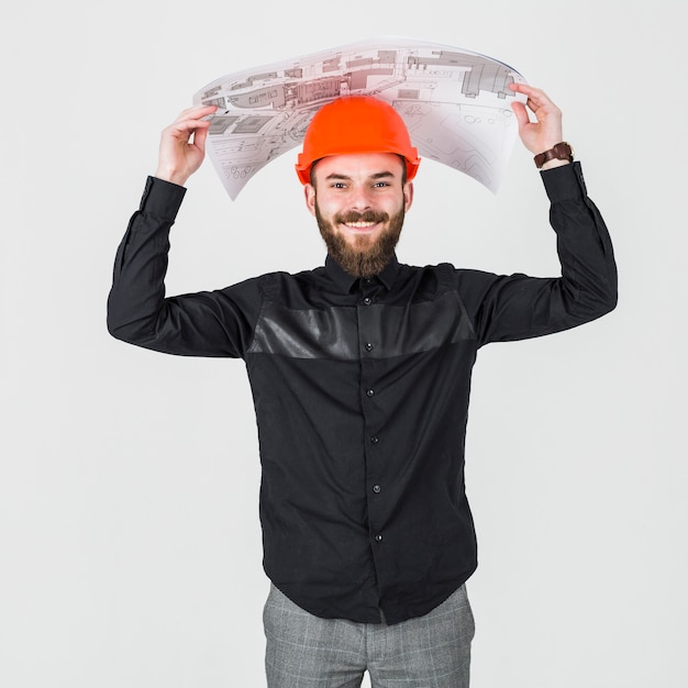 Free photo smiling young male architect holding blueprint over his head