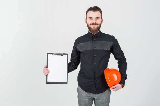 Smiling young male architect holding hardhat and clipboard