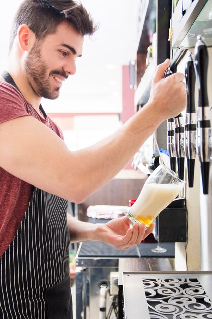 笑顔若い男性のバーテンダーは、タップから新鮮な軽いビールを注ぐ
