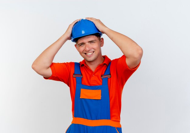 Smiling young male builder wearing uniform and safety helmet grabbed head on white