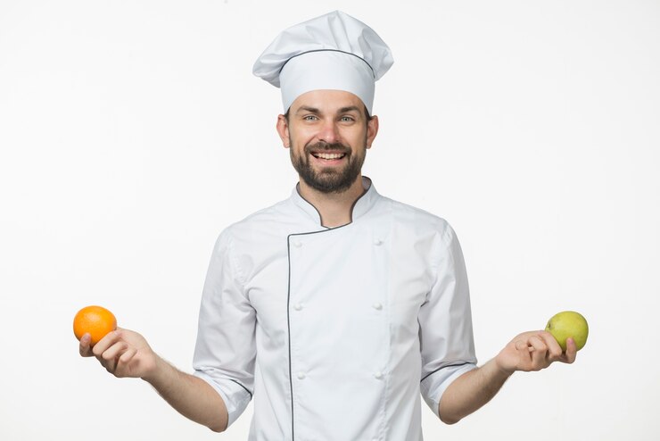 Free Photo smiling young male chef holding and ripe orange and green apple in his hand
