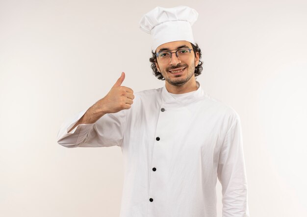 Smiling young male cook wearing chef uniform and glasses his thumb up isolated on white wall