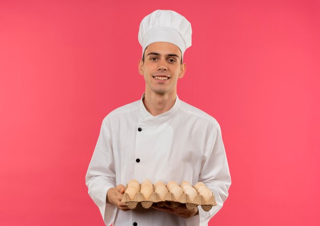 Улыбающийся молодой мужчина-повар в униформе шеф-повара держит партию яиц